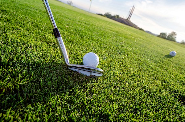 Satter, grüner Rasen, auf dem ein Golfball gerade von einem Golfschläger in Schräglage angestoßen wird