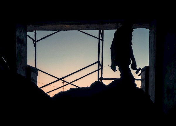 Männliche Person im Schatten am Ausgang einer Bergbaugrube mit Helm und Werkzeug in den Händen