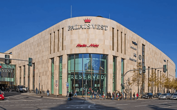 Vordereingang des Palais Vest mit sandfarbener Fassade und roter Krone aus Logo