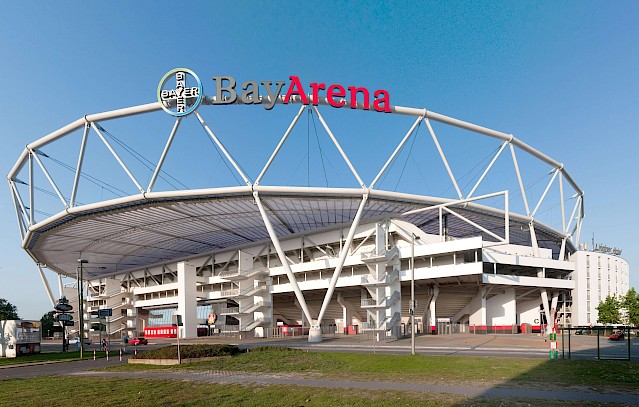 Geometrisch geformte Fassade der BayArena mit großem rot grauem Logo an der Frontseite.